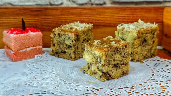 Çeşit çeşit kek dilimleri arasında rendelenmiş peynirli muzlu ekmek ve kırsal ahşap bir ortamda dantel bir altlığa yerleştirilmiş pembe sünger keki de var. Seçici odak