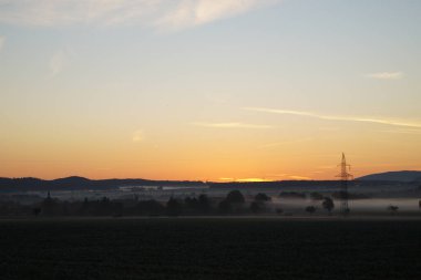 Güneşin doğuşuyla muhteşem bir gün sisli araziyi turuncu / altın bir ışıkla yıkıyor. Tarlaları, ağaçları, köyleri ve dağları görebilirsiniz. Güneşin altında bir sis duvarı vardır..