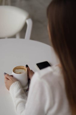 Beyaz kazaklı kız sabah kahvesini içiyor.