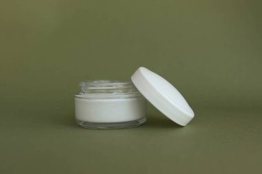 Yeşil arka planda beyaz etiketli yüz kremi için beyaz şişe. Doğal kozmetik ürünü.