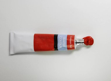 Beyaz bir yüzeydeki tüplerden sıkılmış kırmızı akrilik boya. Tüpün metal bir kapağı var. Boya kalın, desenli boncuklar oluşturuyor. Kremsi bir kıvam ve canlı bir renk sergiliyorlar..