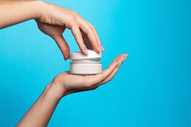 Mavi arka planda krema kavanozu olan kadın elleri. Mavi arka planda bir kavanoz cilt bakım kremi tutan kadın. Mavi arka planda krem tutan kadın, yakın plan. Metin için boşluk