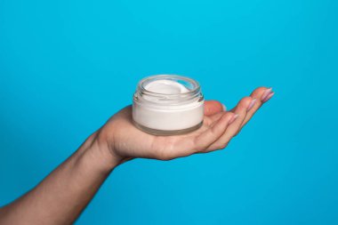 Mavi arka planda krema kavanozu olan kadın elleri. Mavi arka planda bir kavanoz cilt bakım kremi tutan kadın. Mavi arka planda krem tutan kadın, yakın plan. Metin için boşluk