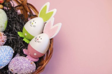 Pembe arka planda tavşan kulaklı pembe bir tavşanlı paskalya yumurtası sepeti içindeki renkli paskalya yumurtaları. Paskalya arkaplanı. Pembe çiçekli bir sepette paskalya yumurtaları. Pembe arka planda paskalya yumurtalarını tutan eller.