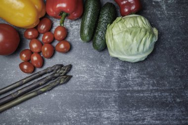 Çiğ organik sebze kompozisyonu. Çiğ organik sebzelerle üst düzey kompozisyon. Üst manzara. Koyu bir yüzeyde taze sebzeler. kuşkonmaz, kiraz domatesleri, dolmalık biber, salatalık lahanası. sağlıklı yeme kavramı