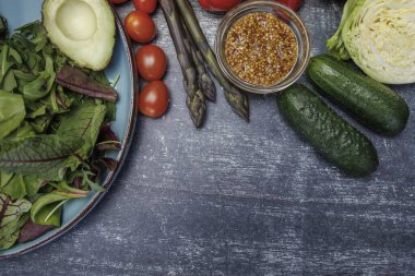 Taze sebzelerden oluşan sağlıklı bir salata ve ahşap masa, üst görüş. Koyu yüzey manzaralı bir tabakta taze sebzeler ve otlar. avokado, kiraz domatesleri, dolma biber, kuşkonmaz, maydanoz ve tahıllı hardal. sağlıklı beslenme endişesi