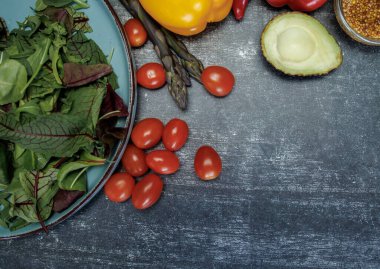 Sebzeli ve yeşillikli taze salata. Taze sebzeler ve siyah yüzey manzaralı bir tabakta otlar. avokado, kiraz domatesleri, dolma biber, kuşkonmaz, maydanoz ve tahıllı hardal. sağlıklı beslenme endişesi