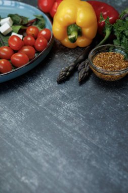 Karanlık bir masada taze sebze ve baharatlar. Vejetaryen yemeği. Taze sebze salatası, yeşillik, dolmalık biberli peynir, kuşkonmaz, hardal tohumu, sağlıklı beslenme.