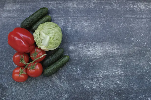 Karanlık bir yüzeyde taze sebzeler yatıyor. Domates, salatalık, lahana, dolmalık biber. Sağlıklı gıda, taze malzeme ve vejetaryen mutfağı kavramı. 