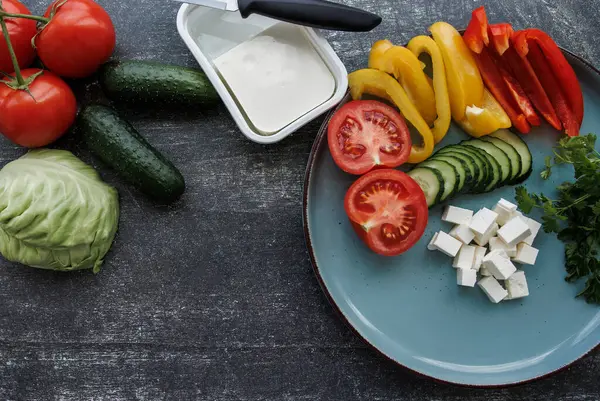 Taze sebzeli ve peynirli salata. Dilimlenmiş taze sebzeli bir tabak. Karanlık bir arka planda çeşitli sebzeler. Sağlıklı bir yemeğin sonu