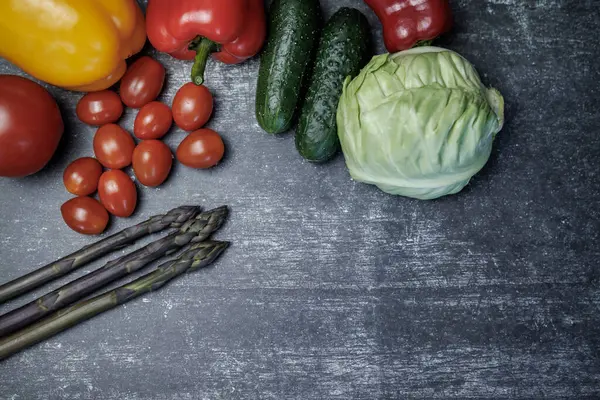 Çiğ organik sebze kompozisyonu. Çiğ organik sebzelerle üst düzey kompozisyon. Üst manzara. Koyu bir yüzeyde taze sebzeler. kuşkonmaz, kiraz domatesleri, dolmalık biber, salatalık lahanası. sağlıklı yeme kavramı