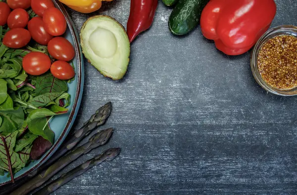 Bir kase taze yeşil organik salata, domatesli, salatalıklı, sarımsaklı ve otlu siyah kırsal masa, fotokopi alanı, düzlük