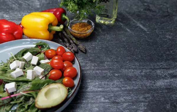 Beyaz bir masada taze sebzeler, sağlıklı vejetaryen yiyecekler. Üzerinde taze sebzeler ve beyaz peynirden salata bulunan karanlık bir taş masanın yatay fotoğrafı. Koyu bir yüzeyde salata, beyaz peynir küpleri ve yeşillikler.