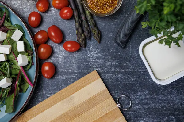 Peynirli ve ıspanaklı salata. Taze yaprak, peynir ve mavi tabakta salata. Kirazlı domates, dolmalık biber, kuşkonmaz taneli hardal, kesme tahtası. Yukarıdan bak. sağlıklı yeme kavramı.