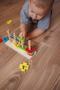Gri tişörtlü küçük çocuk yerde eğitici oyuncaklarla oynuyor. Erken çocuk gelişimi kavramı, oyun oynayarak öğrenme. Renkli geometrik şekiller. oyuncaklara yakın çekim