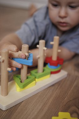 Ahşap eğitici şekil ayırıcı oyuncakla oynayan bir çocuğun yakın çekimi. Ellere ve renkli geometrik şekillere odaklan. Oyun, iyi motor beceriler ve erken çocukluk gelişimi yoluyla öğrenme kavramı