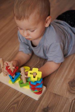 Çocuk yerde yatan eğitici tahta oyuncakla oynuyor. Erken çocukluk gelişimi kavramı, oyun oynayarak öğrenme. Renkli geometrik şekiller. küçük eller