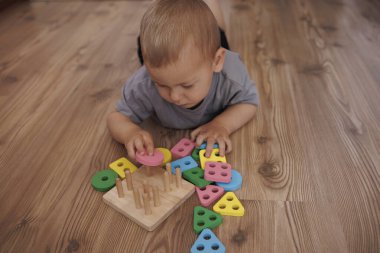 Yürüyen çocuk çiviler üzerinde renkli geometrik şekiller sıralıyor. Küçük çocuk evde eğitici tahta oyuncaklarla oynuyor. Erken çocukluk gelişimi kavramı, oyun ve iyi motor becerilerle öğrenme. Metin için boşluk