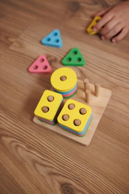 Childs 'ın elleri ahşap zeminde renkli ahşap şekillendiriciyle oynuyor. Bebekler için eğitim oyuncağı, erken öğrenim ve gelişme, iyi motor beceriler, Montessori etkinliği.