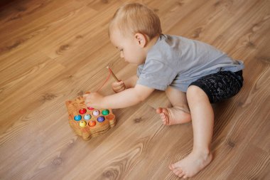 Odada oyuncakla oynayan sevimli küçük çocuk kameraya bakıyor, yerde oturuyor.