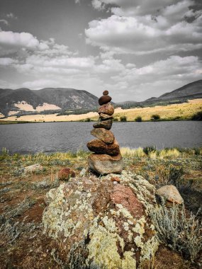 stack of balancing rocks in front of a small lake in the San Juan Mountains on a cloudy summer day clipart