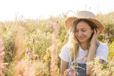 Samimi bir gülümsemesi olan genç bir kadın çiçek tarlasında güneşli bir günün tadını çıkarıyor. Görüntü yazın özünü, özgürlüğü ve doğayla uyumu yakalar.