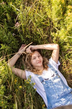 Samimi bir gülümsemesi olan genç bir kadın çiçek tarlasında güneşli bir günün tadını çıkarıyor. Görüntü yazın özünü, özgürlüğü ve doğayla uyumu yakalar.