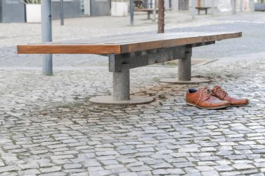 Brown leather shoes on a cobblestone pavement next to a bench in an urban setting. clipart