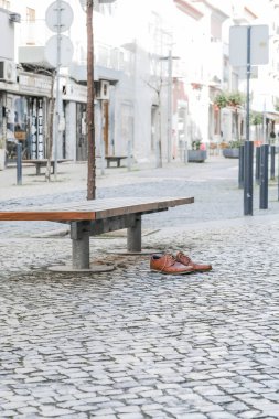 Brown leather shoes on a cobblestone pavement next to a bench in an urban setting. clipart