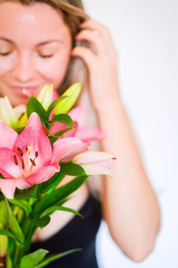 Beyaz arka planda beyaz ve pembe zambaklar tutan bir kadın..