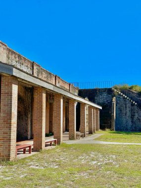 Bir sıra tuğla sütunlar Fort Pickens, Florida 'nın avlusunu çevreleyecek, canlı mavi bir gökyüzünün altında. Açık alan ve tarihi mimarinin karışımı huzurlu ve yansıtıcı bir atmosfer yaratır..