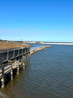 ALE 'nin Veliaht Adası' nda tahta bir tahta kaldırım suyun üzerinde uzanıyor. Sahne, adanın doğal güzelliklerini gözler önüne seren sakin sular, kumlu kumullar ve canlı mavi gökyüzünün altındaki çimenli kıyıları içeriyor..