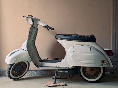 Pacitan, Endonezya - 18 Mayıs 2023: 18 Mayıs 2023 'te Endonezya' nın Pacitan kentinin arka planında krem renkli bir duvar bulunan bir garajda beyaz bir Vespa scooter park etti..