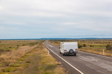 A camper van journeys along a remote road in Queensland's Outback, surrounded by vast landscapes and blue skies. This adventurous setting captures the essence of exploration and travel in Australia. clipart