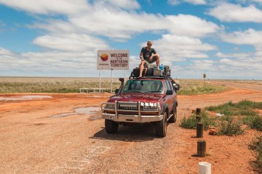 Travelers cheer on top of their vehicle after reaching the Northern Territory, embracing the rugged Australian Outback. clipart