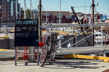 At the harbor in Bodo, Nordland, a hybrid bicycle leans against a welcome sign, inviting visitors to enjoy the beautiful scenery and outdoor activities available in the area. clipart