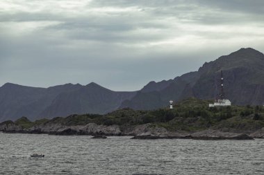 Sakin körfez, Lofoten Adaları 'nın görkemli dağlarını yansıtır. Bulutlu bir gökyüzünün altında büyüleyici bir vahşi doğa ile çevrili küçük bir tekne denizde geziniyor..