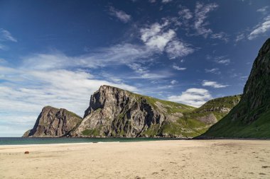 Kvalvika 'nın çarpıcı kıyı manzarası, Norveç' in Lofoten kentinde yumuşak kum ve bulutların üzerinde sürüklendiği sakin bir plajdan keskin bir şekilde yükselen sarp kayalıklara ev sahipliği yapıyor..