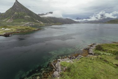 Sakin bir buzul gölü, Lofoten Adaları 'nın yüksek dağlarını yansıtır ve sabah sisi manzarayı kaplar. Canlı renkler doğal güzelliği yansıtıyor.