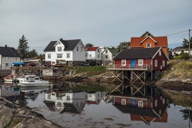 Henningsvr 'deki pitoresk bir liman köyünde, Norveç' in Lofoten Adaları 'ndaki alacakaranlıkta sakin sularda güzel yansıyan kırmızı kulübeler ve tekneler sergilenmektedir.