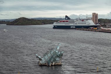 Büyük bir yolcu gemisi Oslo 'nun limanında demirlemiş, yanında da göz alıcı cam bir heykel var. Sudan çıkıp dağlara ve bulutlara çarpıyor..