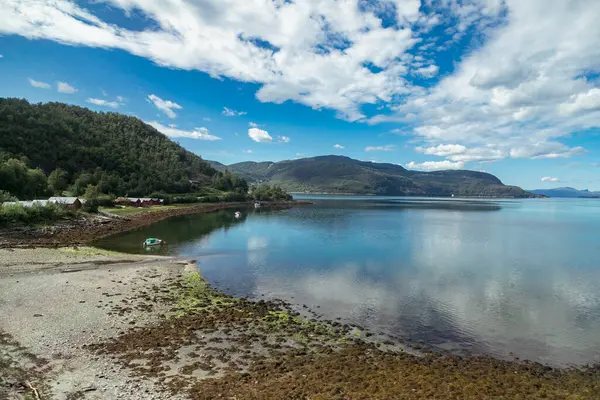 Huzurlu akşam, ağaçların ve dağların sakin sularla buluştuğu, yukarıdaki canlı gökyüzünü ve bulutları yansıttığı, pitoresk bir Norveç kıyı şeridi boyunca uzanır..