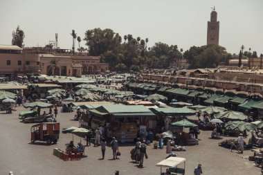 Jemaa el-Fnaa 'nın hareketli pazarı Marakeş' teki satıcılar ve ziyaretçilerle canlanıyor. Çadır kaplı tezgahlarda yiyecek ve mallar sergileniyor, güneşli gökyüzünün altında canlı bir atmosfer yaratıyorlar..