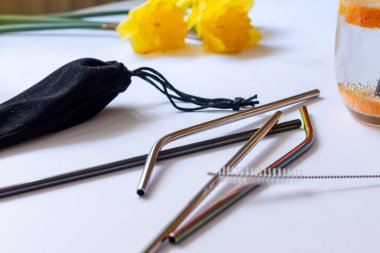 Beyaz bir arka planda, paralı bir çantada, çevre dostu yeniden kullanılabilir pipetler. Arkadaki sarı çiçekler bulanık. Yüksek kalite fotoğraf