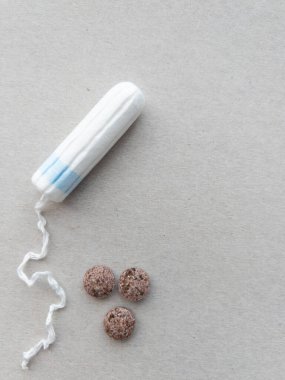 On a simple, neutral surface, a menstrual tampon lies beside three round, brown herbal supplements. The items symbolize a focus on womens health and wellness, particularly during menstruation. clipart