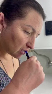 Modern bir banyoda dişlerini titizlikle fırçalayan bir kadın kişisel hijyene olan bağlılığını vurguluyor. Mavi bir diş fırçası kullanıyor, günlük kişisel bakımının bir parçası olarak eksiksiz bir temizlik sağlıyor.