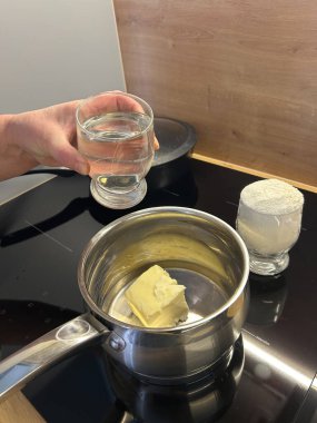 Bir insan bir tencerede tereyağını eritmeye hazırken bir bardak su tutar. Un yakınlarda, pişirmek için alternatif bir turta kabuğunun hazırlandığını gösteriyor..