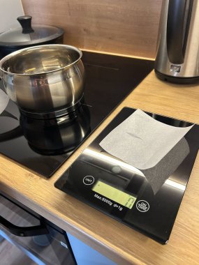 Mutfak düzeneği üzerinde kağıt olan tartı tartısını gösteriyor. Turta hazırlamaya hazır. Yakınlarda bir tencere var. Aktif yemek ya da pişirmeyi gösteriyor..