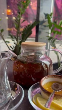 Canlı bitkiler ve sıcak bir atmosferle çevrili bal ve limonla dolu cam çaydanlıkla huzurlu bir deneyimin tadını çıkarın..