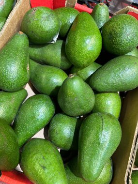 Canlı bir taze, olgun yeşil avokado koleksiyonu ahşap bir sandığın içinde, parlak derilerini ve pürüzsüz dokularını sergileyerek müşterilerin eğlenmesi için hazır bekliyor..